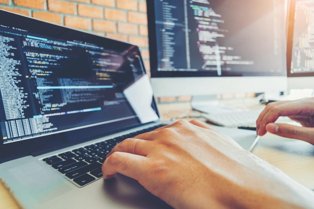 Auf einem Laptop ist Programmquellcode zu sehen, die Hände liegen auf der Tastatur